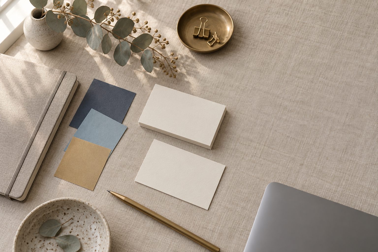 Paper colour swatches, blank business cards and a brass pencil on a linen-covered desk